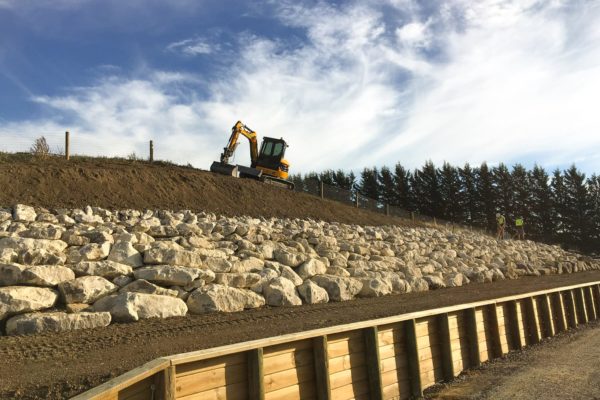 Thornz LandscapesExcavator On Site Finishing Earthworks Job Which Includes Timber Retaining Wall, Large Stone Reinforcement And Land Preparation For Lawn Seed
